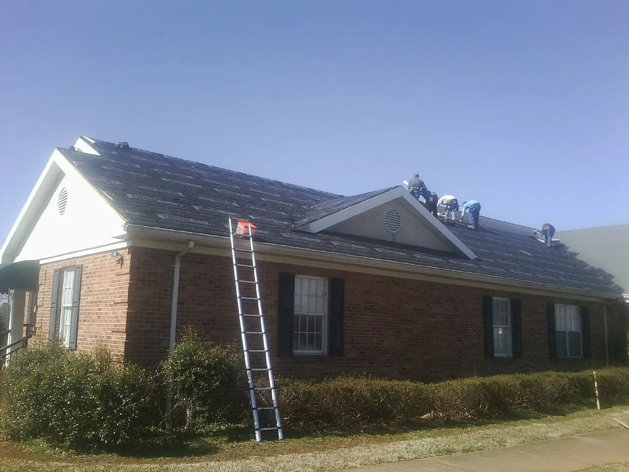 Crew tearing shingles off a brick ranch roof with a ladder set — Emergency Roof Repair work by our crew in Yreka