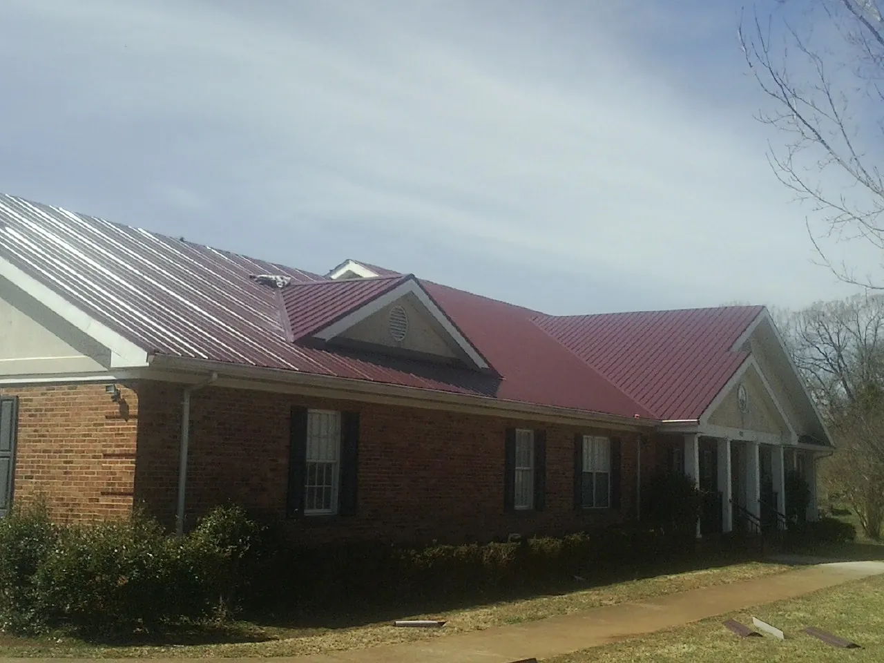 Red metal roof with gabled entries on a long brick building, from a Hail Damage Roof Repair job in Yreka