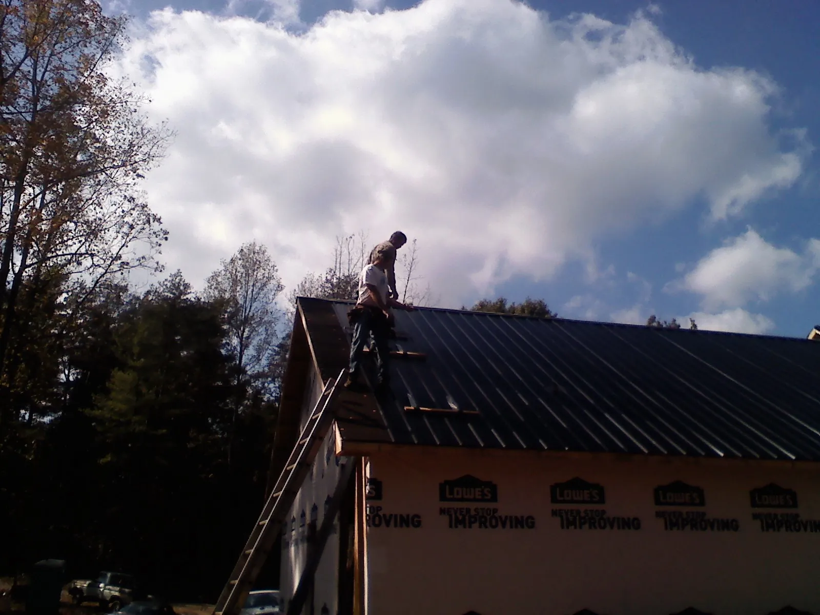 Roofer fastening dark metal panels high against a cloudy sky, from a Roof Inspection job in Yreka
